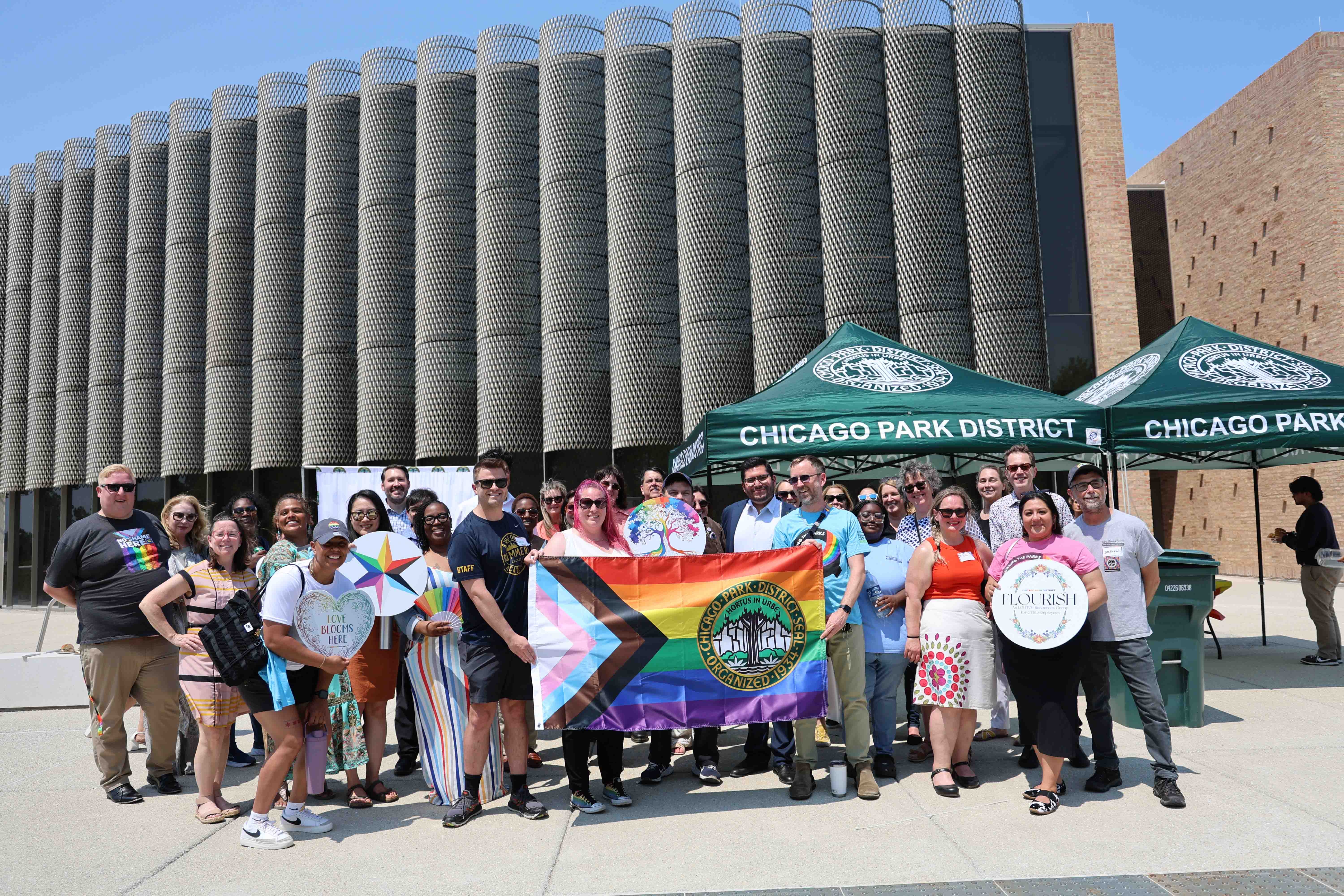 Group photo of Chicago Park District staff holding Pride flag and signs in front of a unique building.